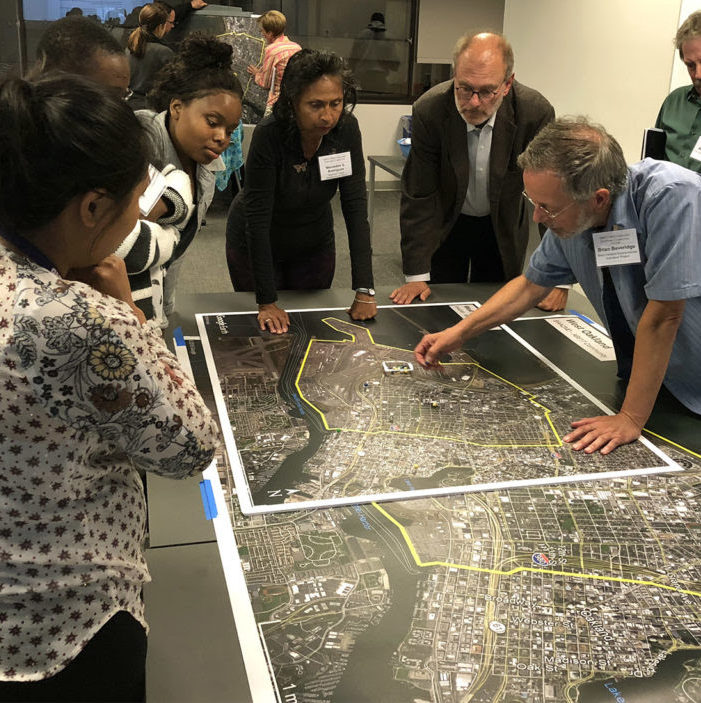 A group of West Oakland residents and policy-makers stand around a table looking at map of their neighborhood