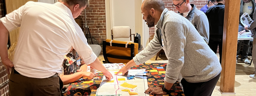 A West Oakland resident and a Link project planner stand over a table covered with a map of the Link covered in sticky notes, pointing to the map and discussing.