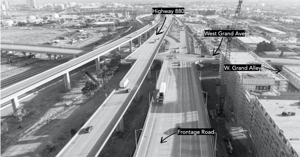 Black-and-white aerial photograph of the elevated highway 880 running top to bottom, with multi-lane Frontage Rd. running alongside at ground level, and West Grand Ave crossing both left to right about midway through the photo.